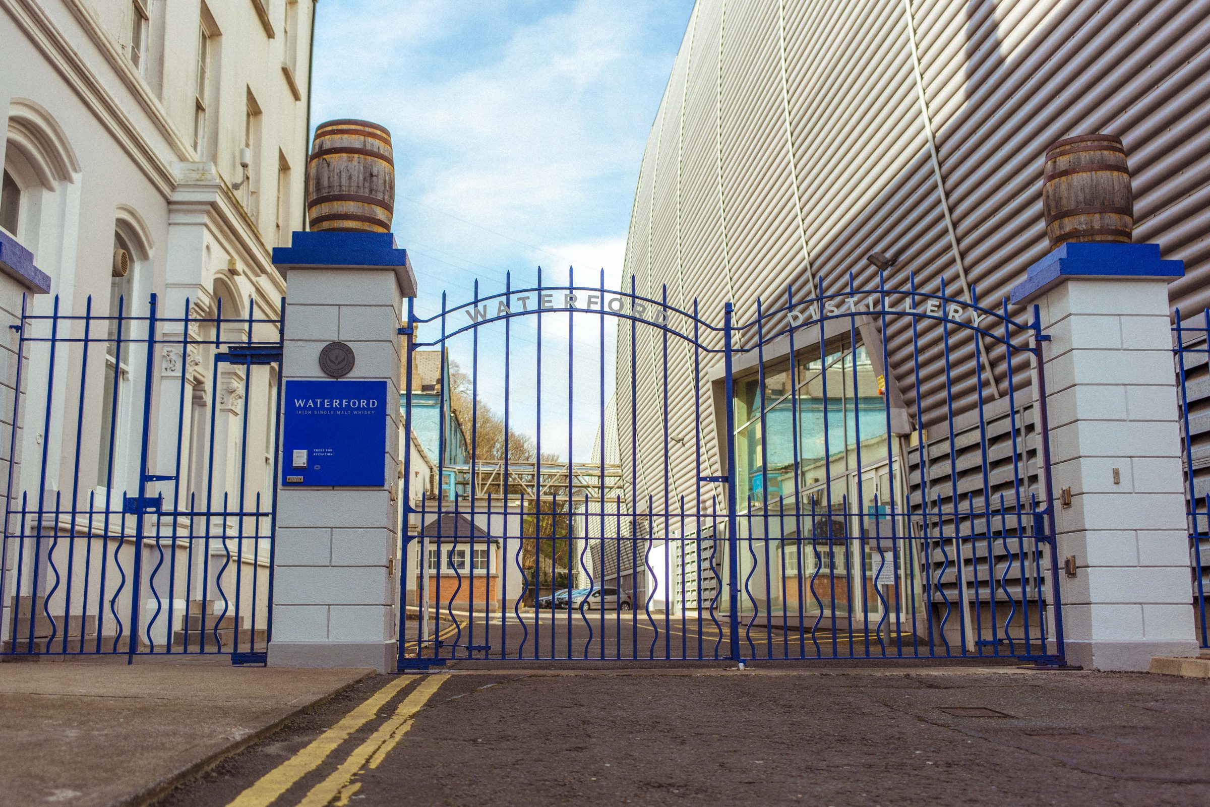 The blue iron gates of Waterford Distillery, a cask on each stone pillar